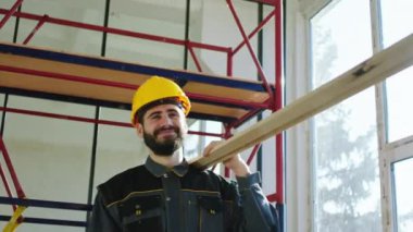 In a sunny day at construction site good looking constructors multiracial with safety equipment carrying a large wood to the other place at construction site. 4k