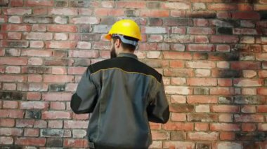 At construction site inside of the building builder man make some measurements of a wall to check if they are straight he wearing safety helmet and uniform. 4k