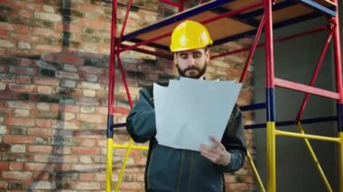 In front of the camera foreman using some plans of construction and design he analysing the schemes and looking to the wall to check if everything it s looking good. 4k