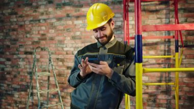 Building man at construction site have a break he using the smartphone to watch something he wearing protective helmet and equipment. 4k