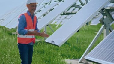 At modern large photovoltaic solar panels the investor man with safety helmet and equipment analysing the photovoltaic solar panels he touching carefully them.