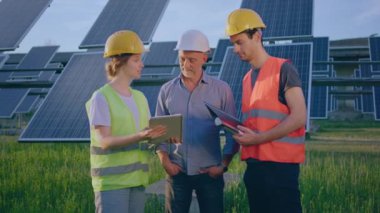Ecological innovation and green energy concept at photovoltaic solar farm the ecological engineer old man and two his assistant discussing about the solar panels using the digital tablet. 4k