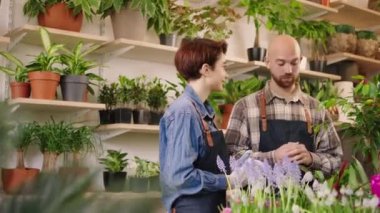 Beautiful woman working as florist in floral store she have a conversation with her colleague sales assistant guy they holding a floral in hands and smiling large. 4k