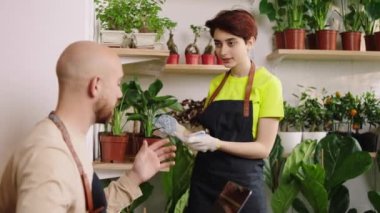 Charismatic florist lady have a conversation with the owner of flowers shop lady holding lady holding flowers on the pot. 4k