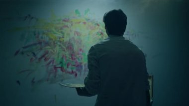 Contemporary art concept the artist man doing a modern artwork on the wall and looking at the picture and analysing the wall. 4k