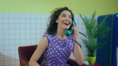 Perfect large smile lady have a conversation on the vintage landline phone while sitting on the sofa in the retro kitchen at home. 4k