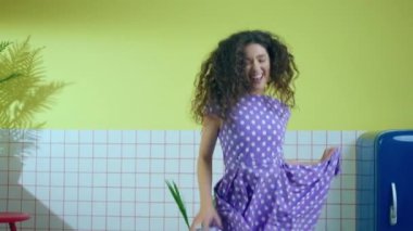 Young looking woman in a beautiful pink dress dancing and moving charismatic in front of the camera in a retro kitchen de star the end she jumping and split legs. 4k