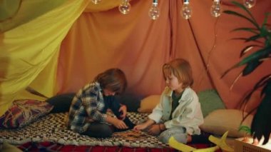 Two boys are laughing and playing together inside a big comfy tent, they re having a lot of fun.