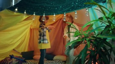 Two boys are really enjoying their time together as they are both laughing and gleefully smiling while dancing together in an indoor hand built tent.
