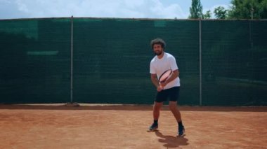 Harika görünümlü profesyonel tenisçi kil sahada maç yaparken tenis topuna raketle sert vuruyor..