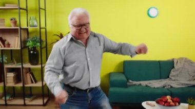 Dancing excited handsome old man in front of the camera while stay at home in living room he enjoy the music and the time speeding alone. Shot on ARRI