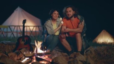 At the campsite in the night romantic couple make some marshmallows on fire and start to eating together hugging with love each other. 4k