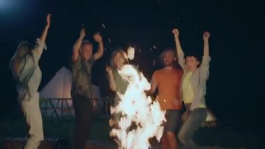 Amazing time at the campsite funny and happy group of friends dancing beside the big fire stake in the night time in the middle of nature. 4k