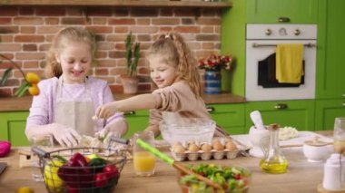 Happy two charismatic kids two little girls at the kitchen island together preparing the dough for a delicious dessert to cook together. 4k