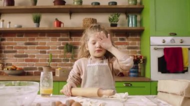 At the modern kitchen island very tired cute girl preparing the dough for a delicious dessert she using the kitchen roller for modelling. 4k