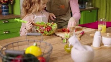 Good looking mother and her beautiful small daughter preparing lunch time together they mixed a healthy salad at the kitchen island.