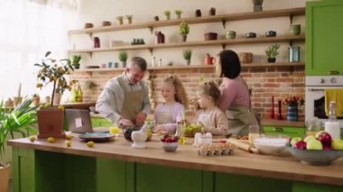 At the modern kitchen island excited mother have fun with her family members playing with salad while preparing the healthy breakfast. 4k