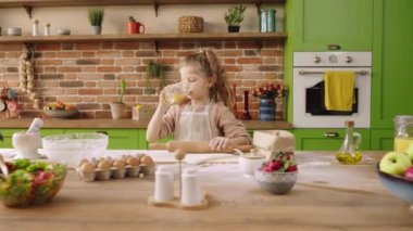 Happy and pretty little girl at the kitchen island using the roller and add some flour over the dough she happy take some juice and drink in front of the camera. Shot on ARRI Alexa Mini