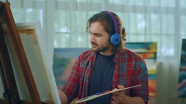 A painter is wearing a very colorful blue set of headphones and listening to music while he paints because it s very soothing. Shot on ARRI Alexa