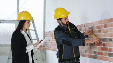İnşaat alanı karizmatik kadın takım elbiseli ve güvenlik başlığı denetçisi güvenlik kaskı takan inşaatçı işçiyle birlikte tazminatı teyit ediyor. 4k