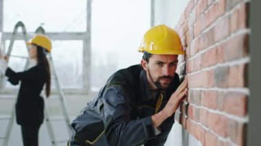 Large spacious construction site concentrated constructor man analysing the walls while a supervisor woman take some pictures of construction with digital tablet. 4k