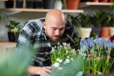 In the floral store the customer guy Caucasian looking take some flowers from the shop shelves and have a conversation with someone on the smartphone.