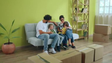 Geniş modern oturma odasında mutlu aile babaları ve iki çocuk yeni bir eve taşınıyor. Kanepede oturup birlikte vakit geçiriyorlar. 4k