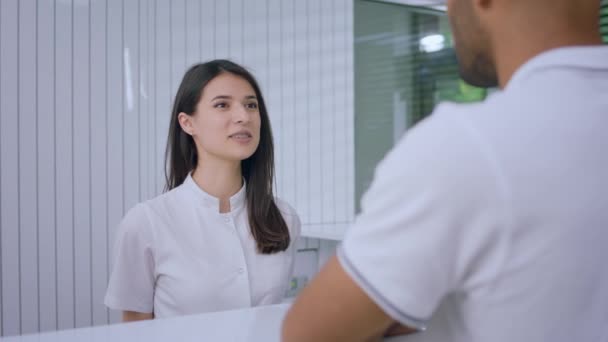 Attractive Young Medical Assistant Reception Desk Discussing Client She Invited — Vídeo de stock