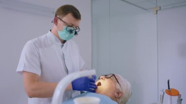 Modern klinikteki yaşlı bir adamın diş çürüklerini tedavi eden profesyonel bir dişçi bu tedavi için özel gözlük takıyor..