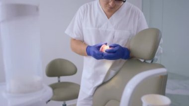 Büyük ve modern dişçi kliniği yakışıklı dişçisi elinde bir diş modelini tutuyor ve sağlık ve dişçilik konseptini inceliyor. 4k