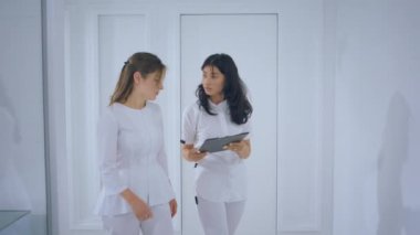 Great looking two medical assistant walking through the medical clinic and discussing something they looking over some map and analysing something in front of the camera. 4k