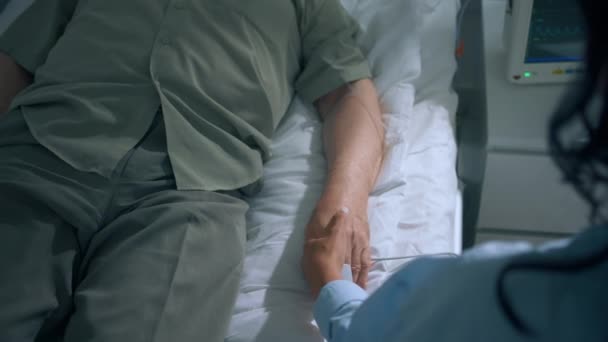 病院の部屋の先輩がソファに横になって休んでいると サポートと慰めを与える彼の手を握って思いやりのある娘を回復します — ストック動画
