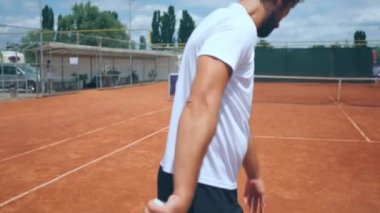 Closeup to the camera taking video of a professional tennis player hitting the ball on the floor outside on the clay tennis court. 4k