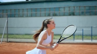 Açık hava tenis kortunda güzel bir kadın raketiyle topa sert vuruyor şampiyonluk için antrenman yapıyor beyaz üniforma giyiyor..