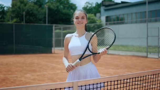 テニスコートの屋外カメラの前でポーズをとっている可愛い女性テニス選手がラケットを手に持ち かわいい笑顔 — ストック動画