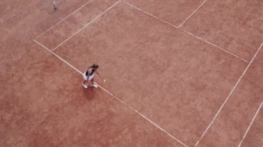 Taking video with drone birds eye view good looking tennis player woman get ready to start the match she hitting the ball with the racket.