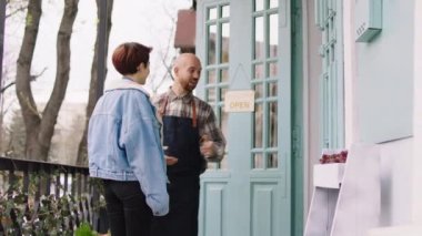 Owner and entrepreneur man invited the customer to his shop outside he have a discussion with the customer lady. 4k