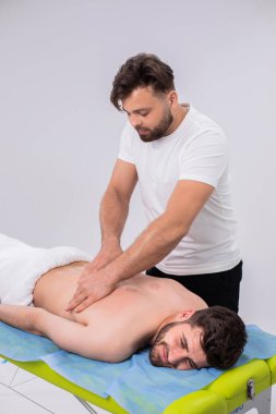 At spa salon the professional masseur doing back revitalising massage the client happy looking to the camera and smile while laying down on the massage table. Portrait