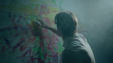 Stüdyodaki duvarda yağlı resim yapan inanılmaz yetenekli bir sanatçı paletten yağlı boya rengini parmaklarıyla alıyor ve resme ekliyor. 4k