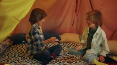 Two young boys with long hair are high fiving each other and seem really happy to be in an indoor tent.