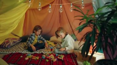 İki çocuk bir çarşaf çadırında birlikte oynarken birbirleriyle konuşup eğleniyorlar..