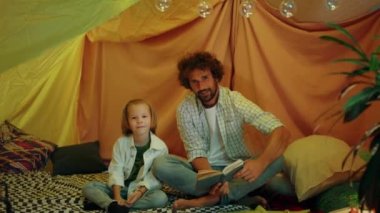 Kameranın önünde, evdeki çadırda kitap okurken kameraya poz veren bir baba ve oğlunun videosunu çekiyorum. 4k