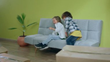 Heyecanlı çocuklar ve aileleri yeni bir eve taşınıyorlar mutlu bir şekilde kanepede oturuyorlar ve hayattaki yeni yerlerinin tadını çıkarıyorlar. Heyecanlanıyorlar. 4k