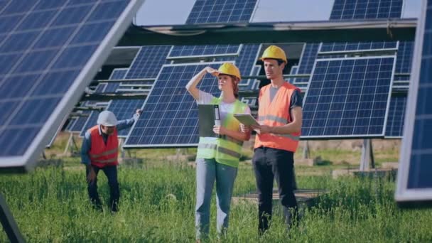 可再生能源的概念和生态环境小组的工程师年轻团队一起分析光伏太阳能电池板的清洁度 他们都戴着安全设备和头盔 开了一枪 — 图库视频影像