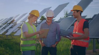 Ekolojik yenilik kavramı ve yeşil enerjili mutlu kadın ekoloji mühendisi ve iki yatırımcı fotovoltaik güneş çiftliğinde gelecek üzerine çalışma planı hakkında tartışıyorlar. 4k
