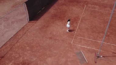 Tenis kortunun önünde, tenis raketiyle topu yakalayan güzel tenisçi kadının kuş bakışı videosunu çekiyorum. 4k