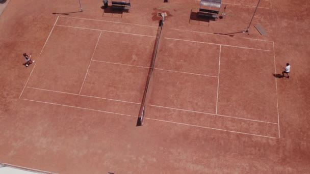 鳥の目をしたドローンビデオ2人のプロのテニス選手の女性と男性は 大きなテニスコートの屋外で晴れた日にテニスの試合を持っています — ストック動画