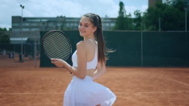 Açık hava kil sahası kameranın önünde büyük bir gülümseme ile güzel bir bayan poz veriyor profesyonel spor raket konseptini tutuyor. 4k