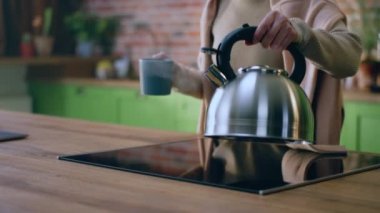 Kameraya yakın büyük bir tasarım mutfak kadını elektrikli ocaktan su ısıtıcısını al ve çay fincanına biraz kaynar su ekle. 4k