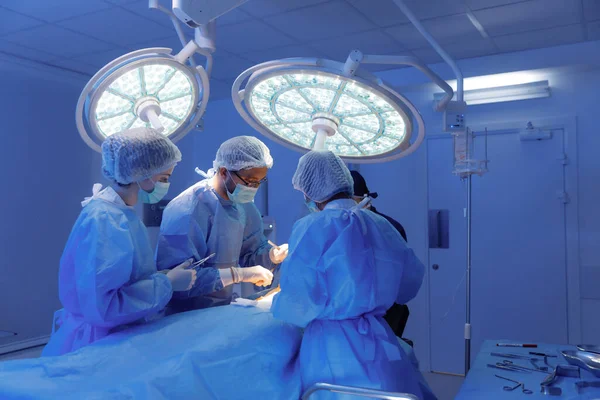 Trzech Lekarzy Fartuchu Jeden Czele Pacjenta Ciemnoniebieskim Fartuchu Operują Rozmawiają — Zdjęcie stockowe